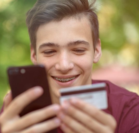 Happy young man is using smartphone and bank card for online shopping